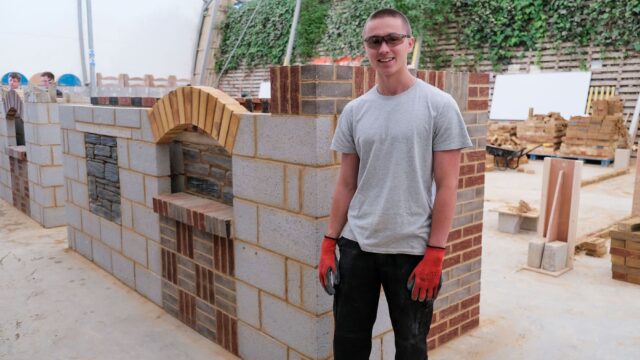 A student stands next to his bricklaying project which shows a variety of different bricklaying techniques.