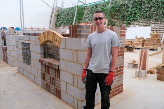 A student stands next to his bricklaying project which shows a variety of different bricklaying techniques.