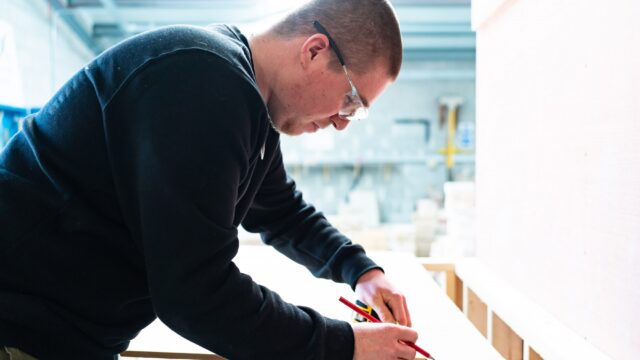 A student with a pencil in hand measuring a wooden block.