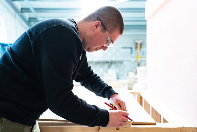 A student with a pencil in hand measuring a wooden block.