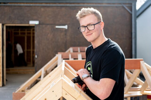 A student using a power drill on a wooden structure.