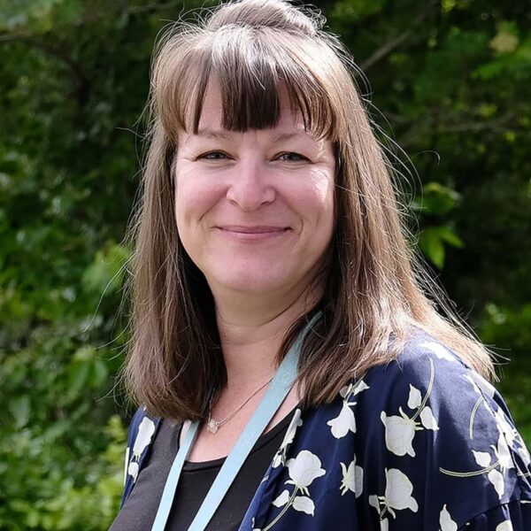 A photo of Caroline smiling. She is wearing a black top with a blue shirt and is wearing her staff lanyard.
