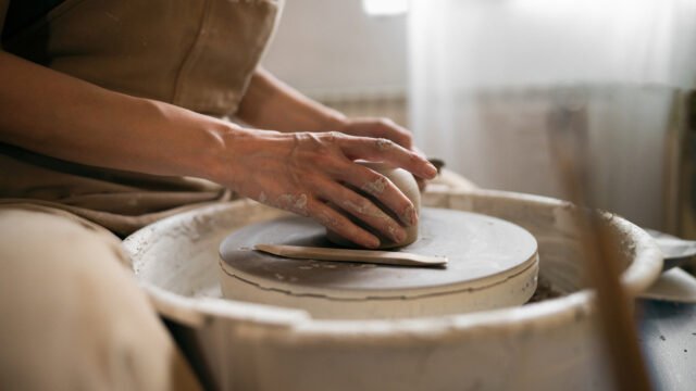 Unrecognizable female ceramics maker or potter working with pottery wheel in workshop.