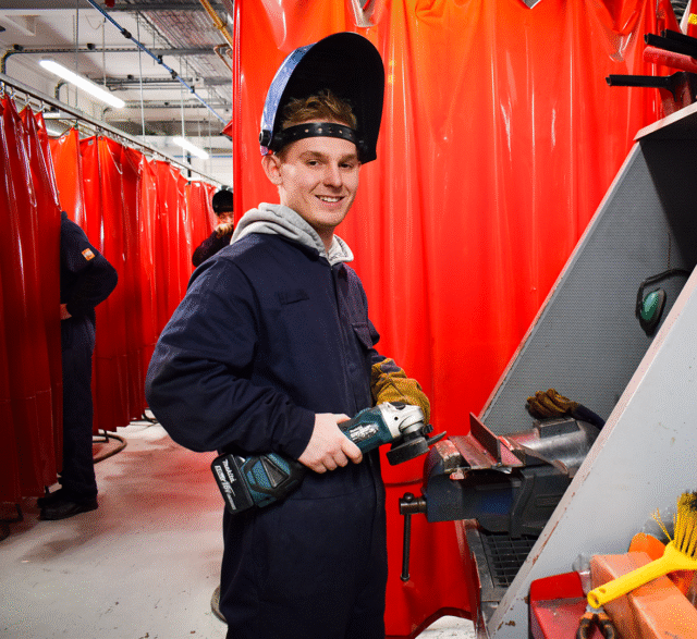 A student is wearing overalls and a welding mask.