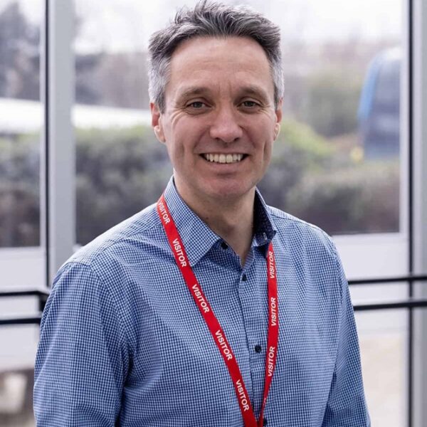 A portrait photo of Chris Wathern, he is stood inside wearing a blue shirt and a visitors lanyard.