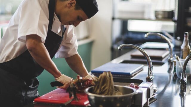 A chef cutting meat in a kitchen.
