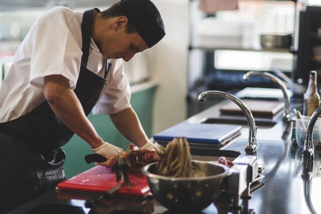 A chef cutting meat in a kitchen.