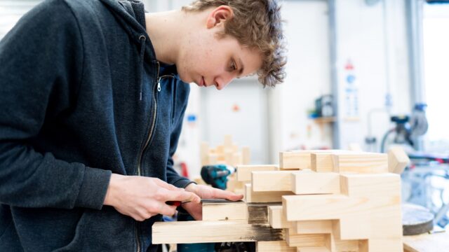 A construction student measuring wooden blocks.
