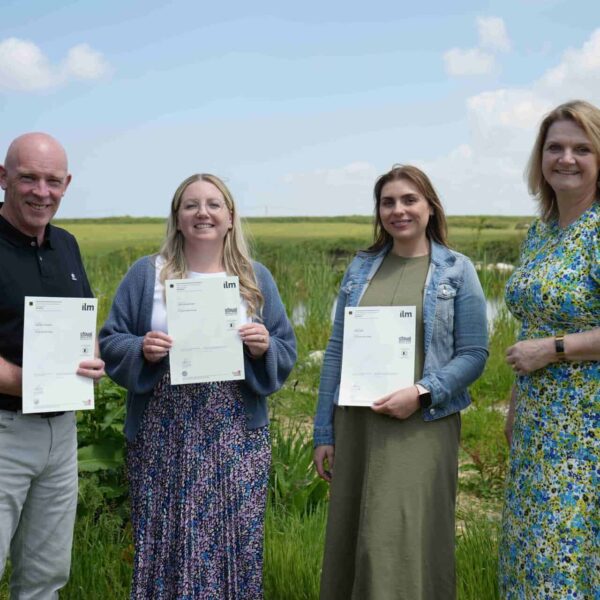 Adult students stand holding up certificates.
