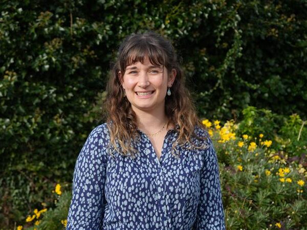 A woman smiles stood outside in a garden.