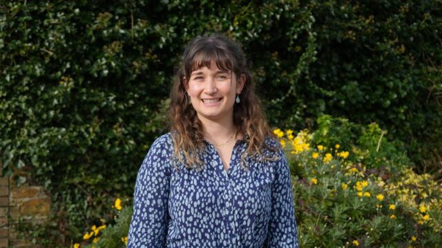 A woman smiles stood outside in a garden.