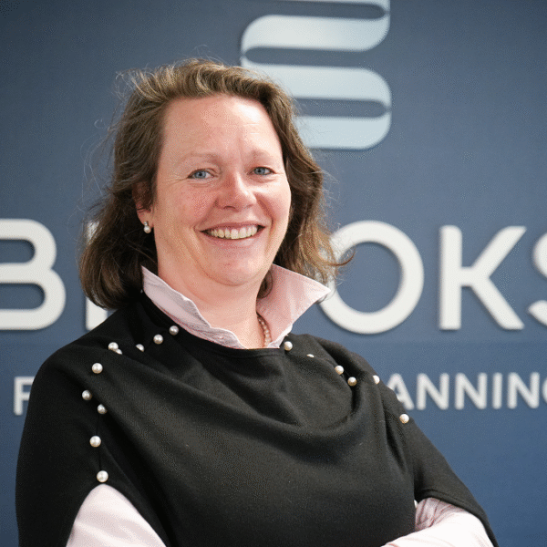 A woman dressed smartly stands in front of a sign that says Brooks Financial Planning.