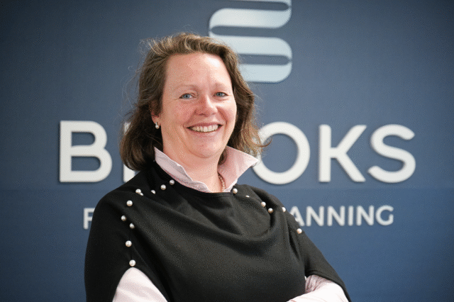 A woman dressed smartly stands in front of a sign that says Brooks Financial Planning.
