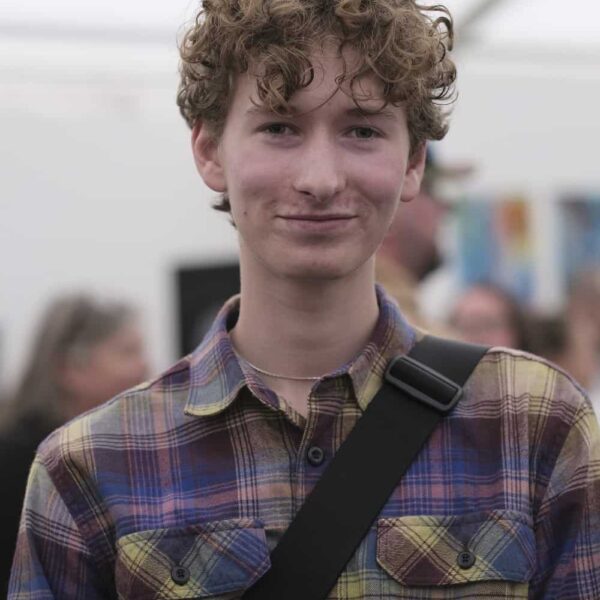 A student with curly hair, a check shirt and cross body bag.