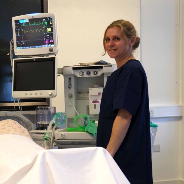 Elly in scrubs next to a hospital bed.
