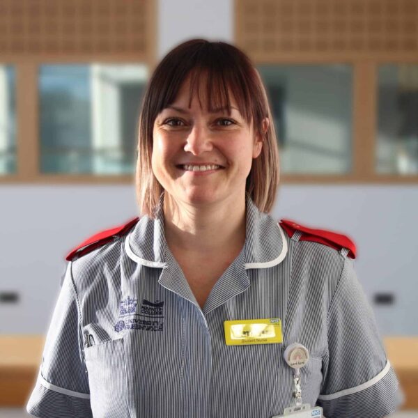 Emma is dressed in a nurses uniform and is wearing ID badges.