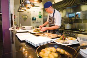 A student chef is putting food onto plates in the Spires Restaurant at Truro College.