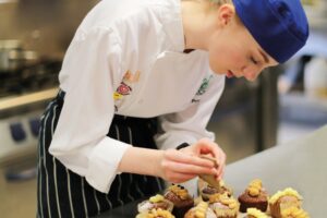 A student piping frosting onto cupcakes.