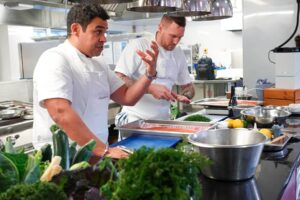Paul Ainsworth giving a cooking demonstration. There are bowls and trays and food in the professional kitchen.