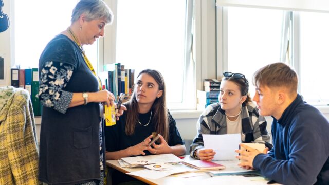 A group of students sat at a classroom table look up at their tutor.