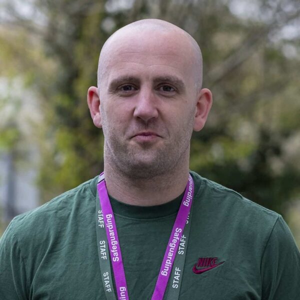A photo of Gary. He is wearing a green top and two staff lanyards.