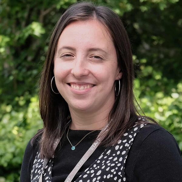 A photo of Gemma smiling. She is wearing a black top with her staff lanyard.