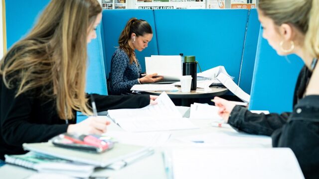 Students sit in the Fal building studying with papers and folders around them.