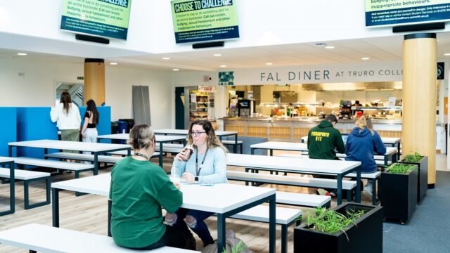 Two students sit at a table in the Fal building canteen enjoying cold drinks.