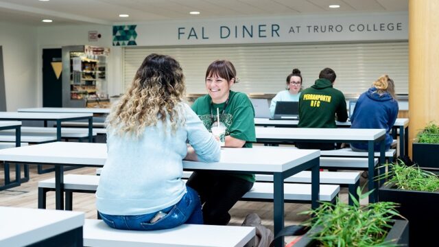 Two adult students sit in the Fal building canteen at the University Centre Truro and Penwith enjoying a starbucks drink and chatting.