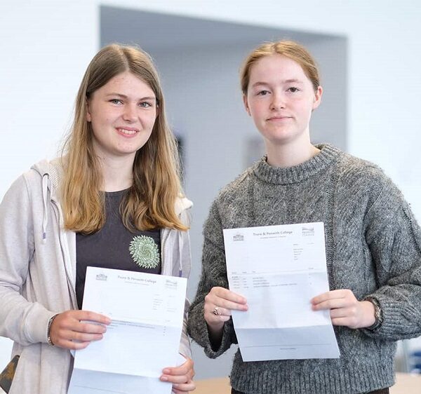 Grace and Martha are holding up their exam results and smiling at the camera.