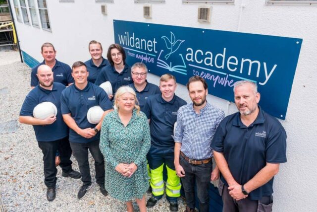 Workers from Wildanet stand outside in their uniforms. A sign that says Wildanet behind them.