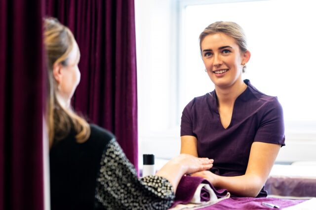 A hair and beauty student wearing a purple tunic is doing a treatment on a client.