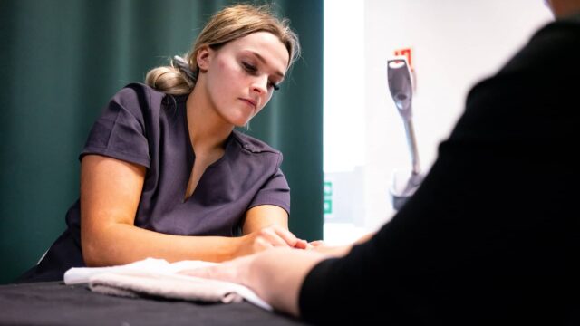 A hair and beauty student doing a hand treatment on a client.