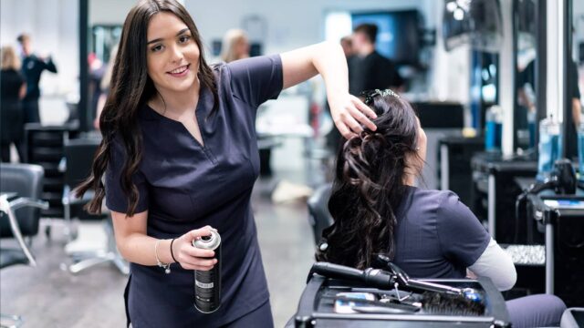 A hair student is spraying hair spray into another student's hair.