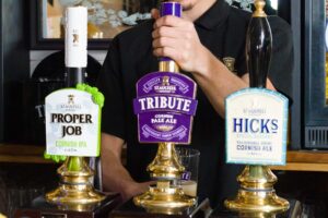 A person working at a bar pouring a pint of Tribute.