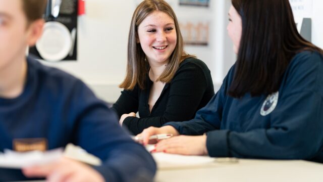 Students sat together at classroom tables smiling.