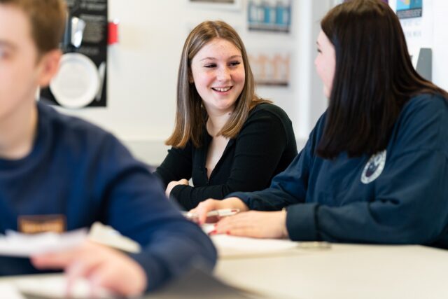 Students sat together at classroom tables smiling.