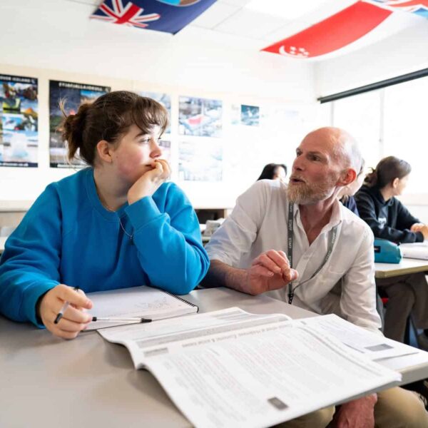 A tutor speaking to a student who has notebooks open in front of them.