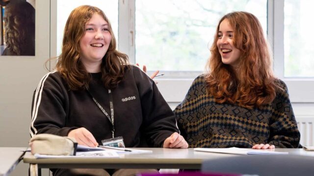 Two students sat at a classroom table laughing.