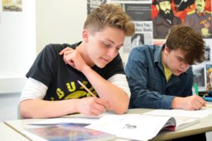 Students working at classroom tables with pens and paper.