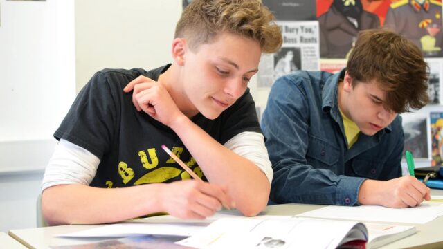Students working at classroom tables with pens and paper.
