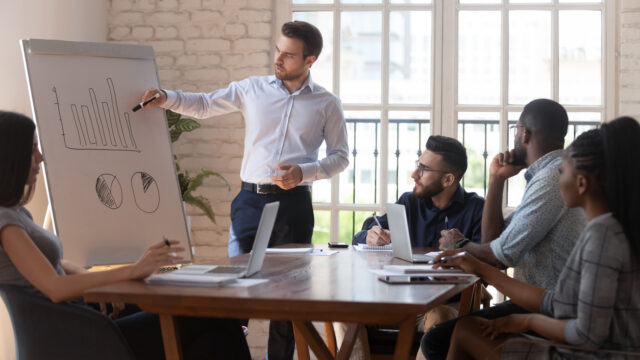 Team leader explains graph strategy during corporate meeting seminar in modern light boardroom.