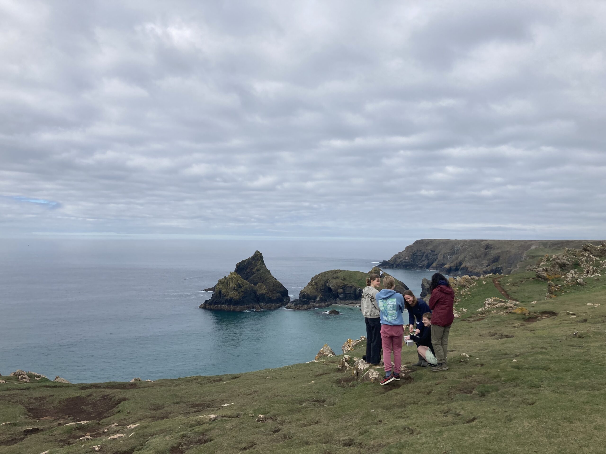 Five students stand in a group on a coastal cliff. You can see the sea and a large grey sky behind them.