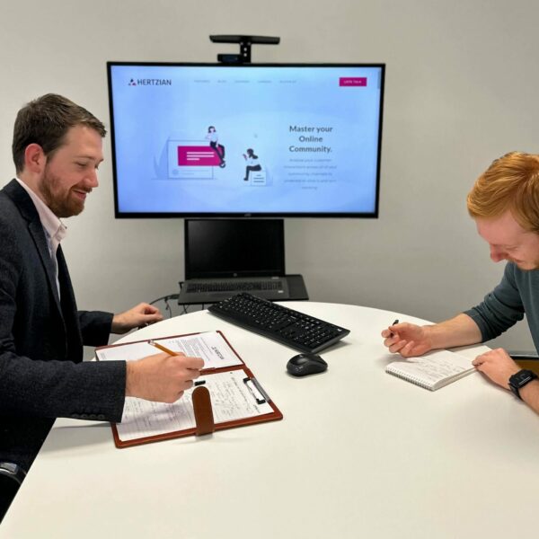 Two people sat opposite each other with a computer between them that says Hertzian.