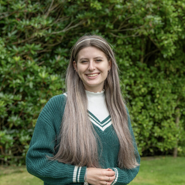 Milarna has long hair and is wearing a green jumper.