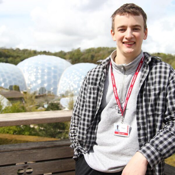 Tom leant against a fence with the Eden Project biomes behind him.