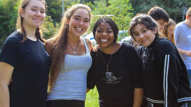A group of students put their arms around each other and smile.