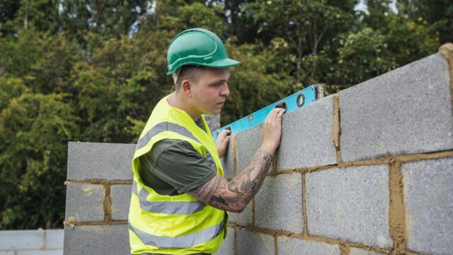 A shot of a spirit level being used to check some brickwork by a male construction worker.