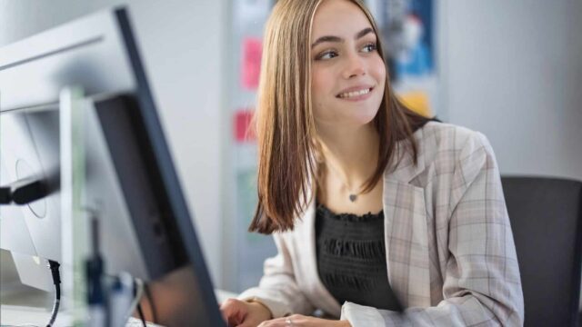 A business woman sat at a computer looking over her shoulder.