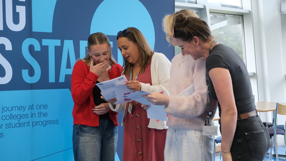 Two students and two staff members look at their results together. They are smiling.